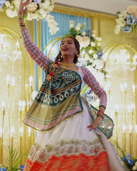 A woman in a colourful lehenga dancing with one arm raised
