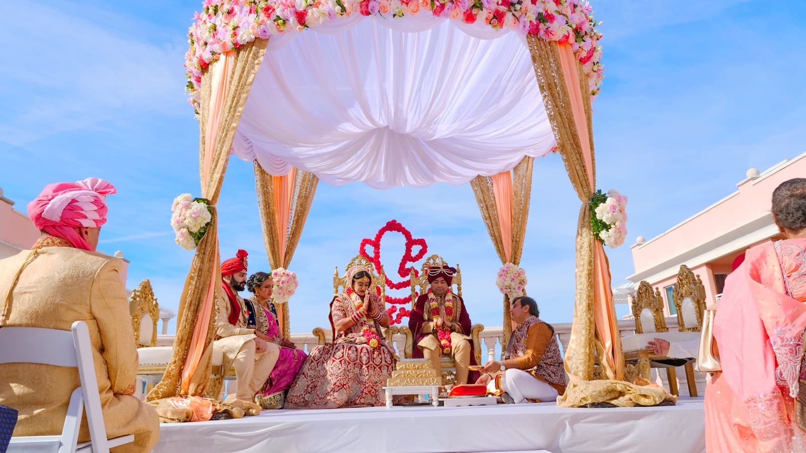 A couple in traditional wedding attire sitting under a floral canopy during a ceremony