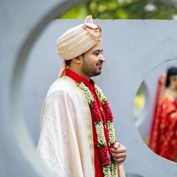 Woman in green, gold, and red sari dress hiding her right eye while smiling