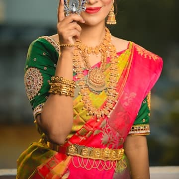 Woman in green, gold, and red sari dress hiding her right eye while smiling