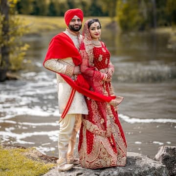 A couple in traditional Indian wedding attire standing on a rock by a river